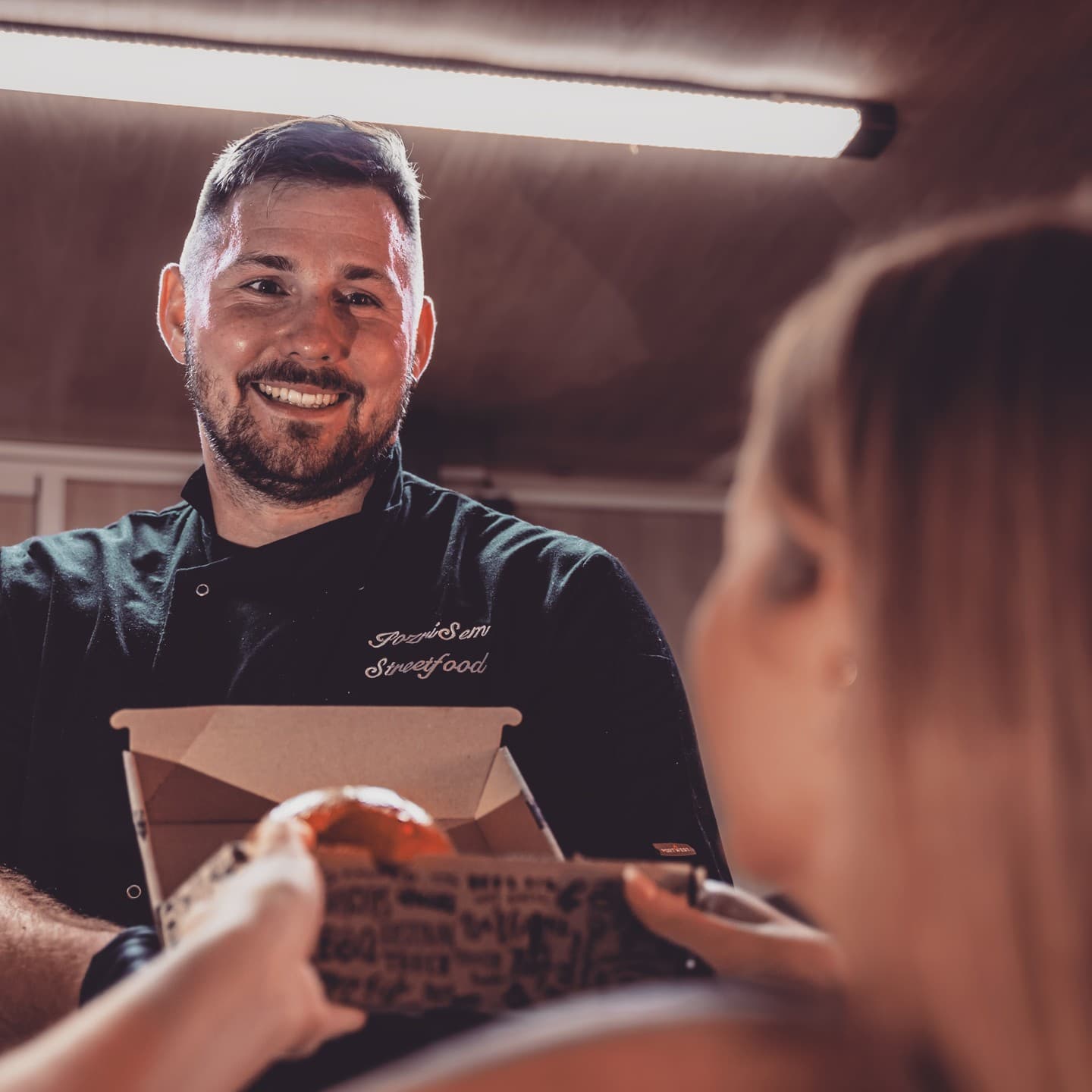 Jakub, kuchár Pozri Sem, podáva jedlo zákazníčke pri foodtrucku v Novej Bani